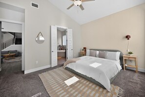 Ein Schlafzimmer mit einem Bett, einem Nachttisch, einer Stehlampe, einem Deckenventilator, einer Tür und einer Treppe zu einem anderen Raum.
