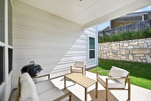 Eine überdachte Terrasse mit Grill, Gartenmöbeln und einer Steinmauer.