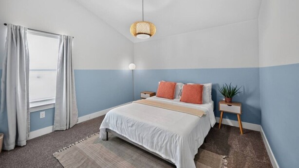 A bedroom with a bed, bedside tables, a hanging light fixture, a window with curtains, and a view. - Modern 4BR, Sleeps 10, King Suite, Home Office, Garage Gym & Game Room (Manor)