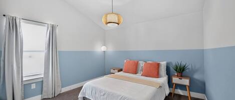 Un dormitorio con cama, mesitas de noche, lámpara colgante, ventana con cortinas y vistas.