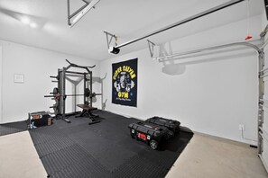 Ein Heimfitnessraum mit Hantelbock, Bank und Gewichtsplatten; ein Banner an der Wand; und eine an der Decke befestigte Klimmzugstange.