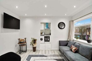 Ein modernes Wohnzimmer mit einer Couch, einem Flachbildfernseher, einer Küchenzeile und einer Wanduhr.
