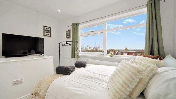 A bedroom with a bed, a television on a stand, a window with curtains, and a view of buildings outside. - Belvedere 4-Bed Apt, Sleeps 9 with Parking (Belvedere)