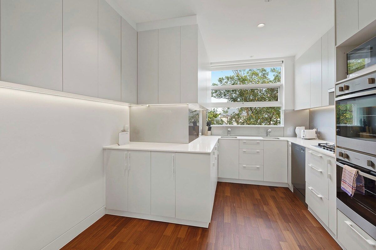 A modern kitchen with white cabinetry, a built-in oven, and a window providing natural light.