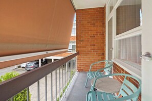 A balcony with a brown awning, a brick wall, and a window with curtains. - Domi Rentals - The Meadow Apartment (Saint Kilda East)