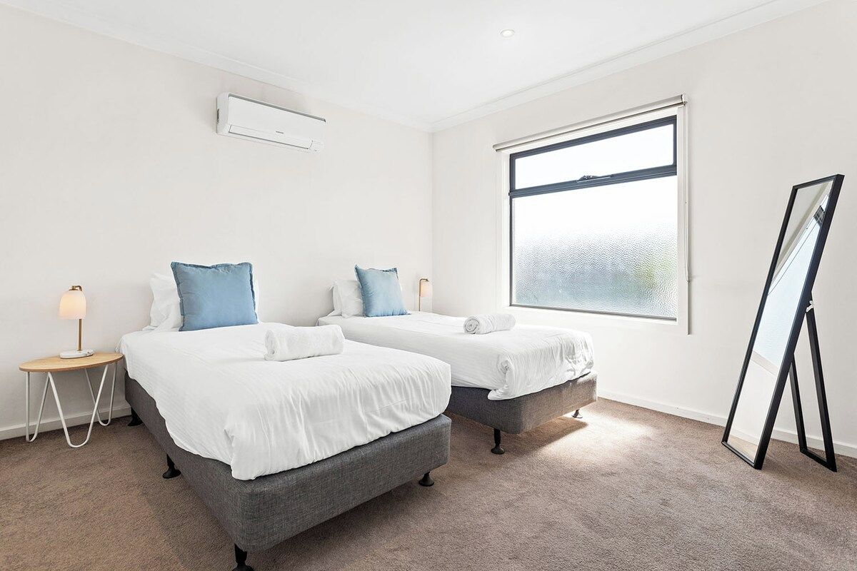 A hotel room with two beds, a standing mirror, and a large window.