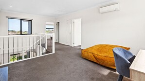 Una camera moderna con una scala, un letto con un cuscino color senape, una scrivania e una finestra con vista.