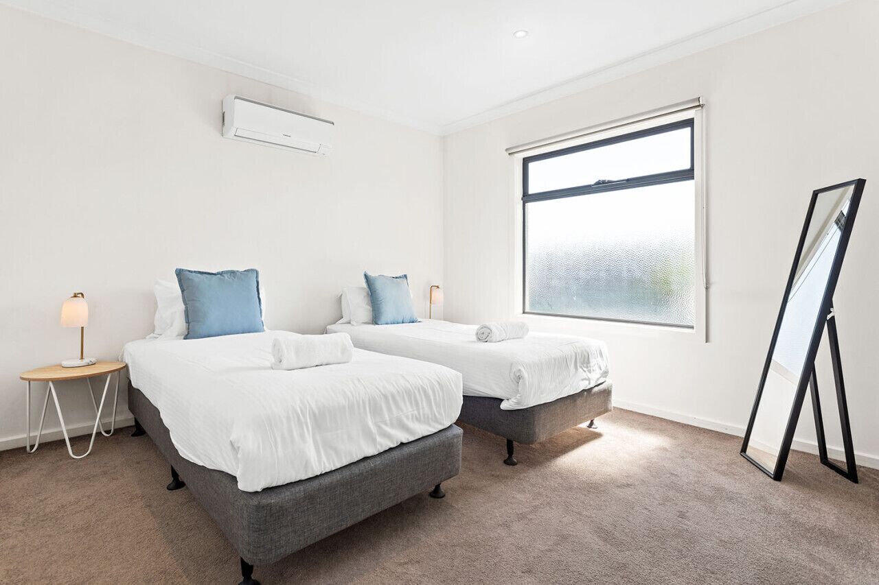 A hotel room with two beds, a standing mirror, and a large window.