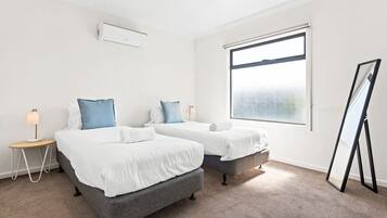 A hotel room with two beds, a standing mirror, and a large window.