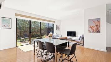 A modern living space with a glass dining table, comfortable seating, and a TV.