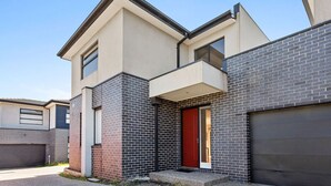 Una moderna casa a due piani con una porta rossa, un garage e un piccolo portico.