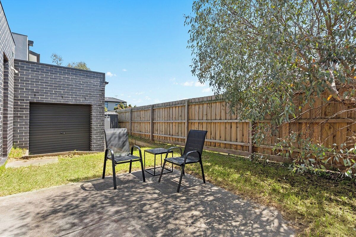 A backyard with a patio, two chairs, a table, a wooden fence, and a garage.
