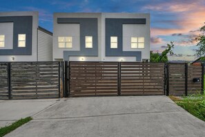 A modern two-story house with a gated driveway and a concrete pathway leading to the entrance.