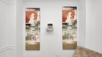 Een kamer met twee grote schilderijen aan de muur, een projector in het plafond en een zachtbeige plaids op een bank.