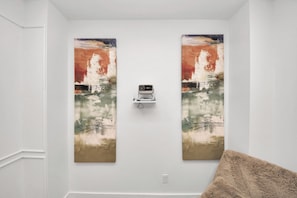 A room with two large paintings on the wall, a ceiling-mounted projector, and a fluffy beige throw pillow on a couch.