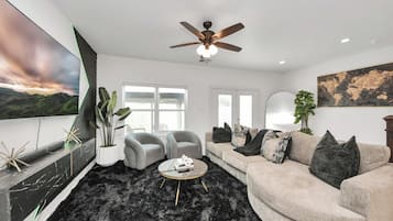 Een moderne woonkamer met een bank, fauteuils, een salontafel en een plafondventilator.