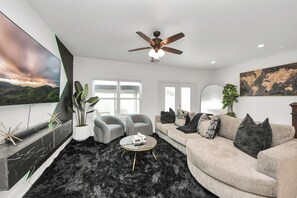 A modern living room with a sofa, armchairs, a coffee table, and a ceiling fan.