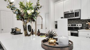 Een moderne keuken met witte kasten, een roestvrijstalen magnetron en een groot eiland met een witte kaars en decoratieve objecten.