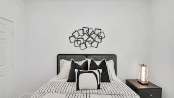 Een slaapkamer met een bed, kussens, een nachtkastje en een wanddecoratie.
