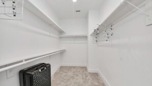 Een schone, witte kamer met vloerbedekking, een zwarte koffer en een witte wandplank met haken.