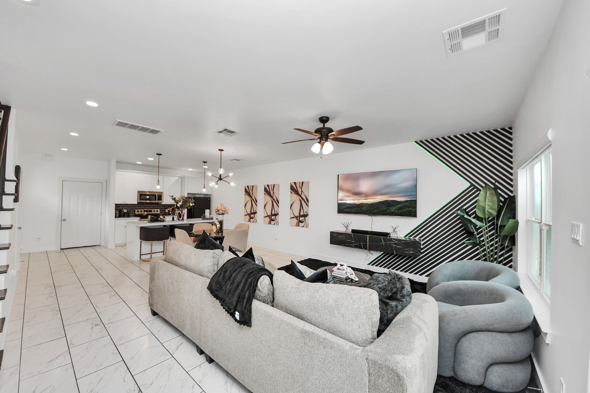 A modern living room with a sofa, a coffee table, and a staircase with a striped wall.