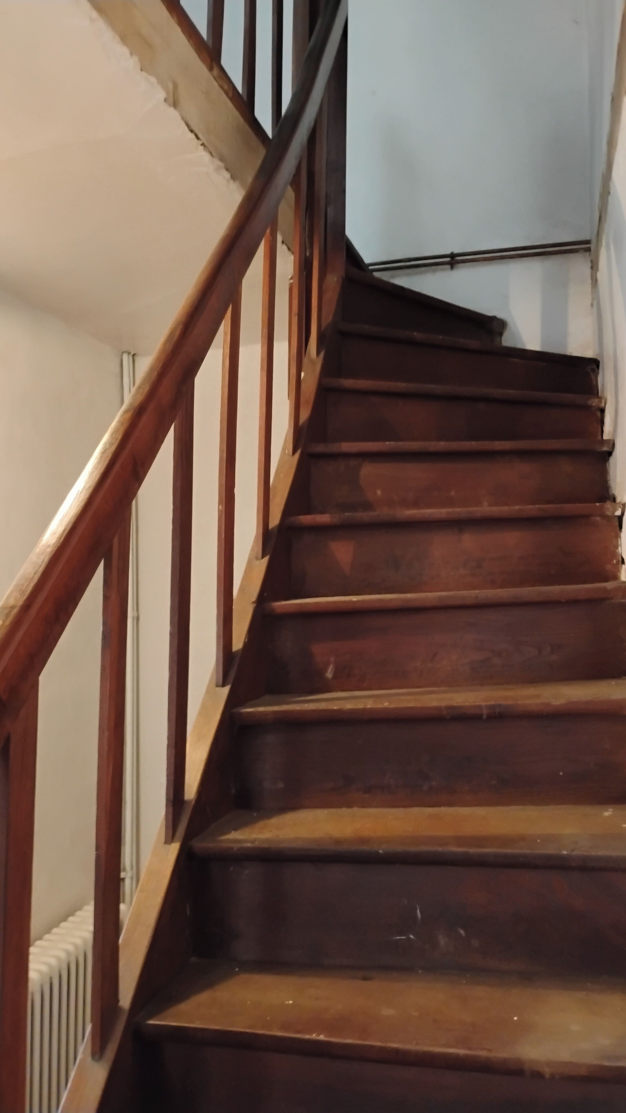 Un escalier en bois avec une rampe métallique menant à un palier.