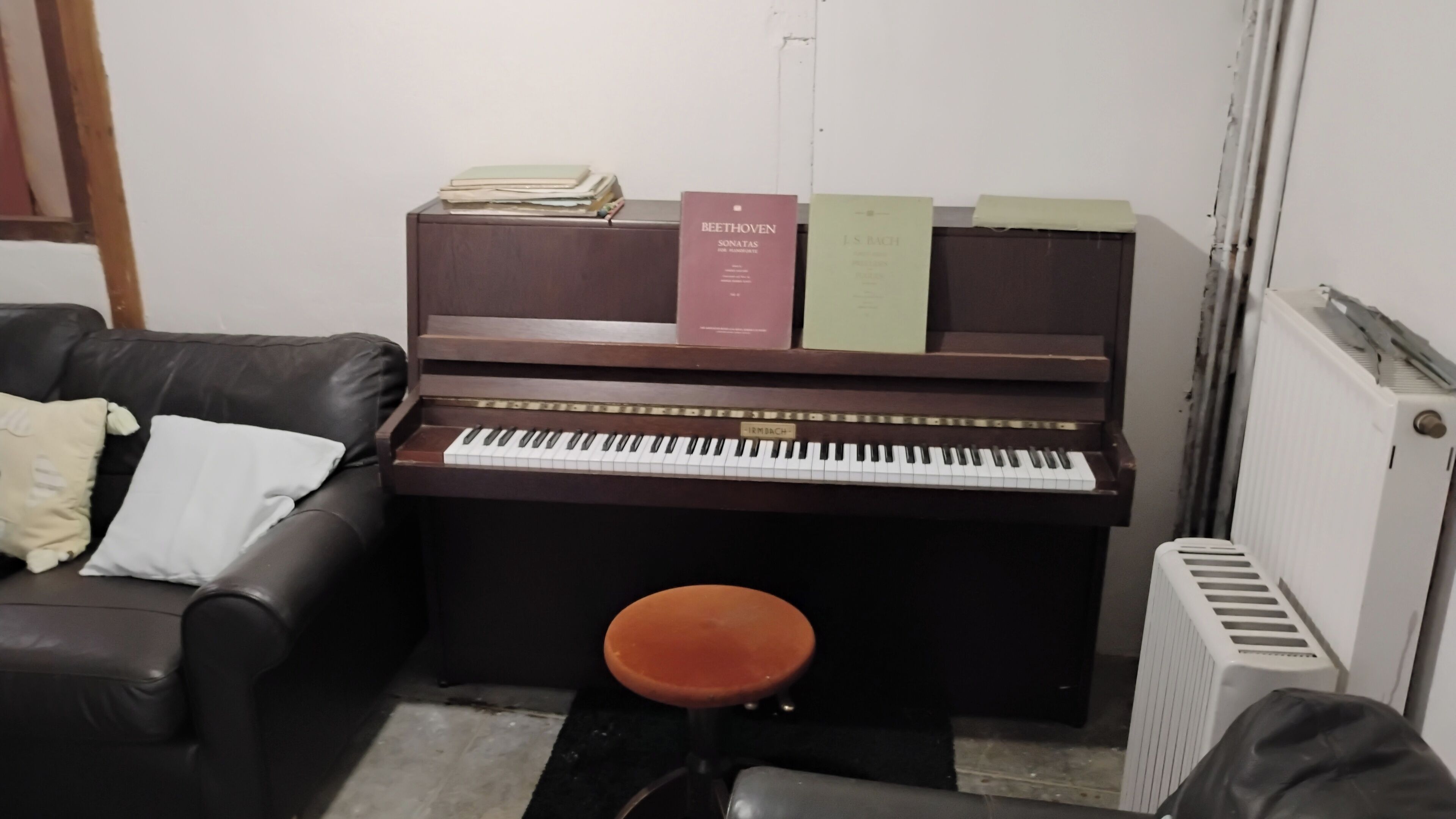 A piano with sheet music, a stool, a couch, and a radiator.