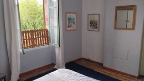 Ein Zimmer mit einem Bett, einem Fenster mit Blick auf Grünflächen und zwei gerahmten Bildern an der Wand.