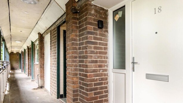 A corridor with brick pillars, white doors numbered 18, and a metal handrail. - Manchester City Short Let (Manchester)