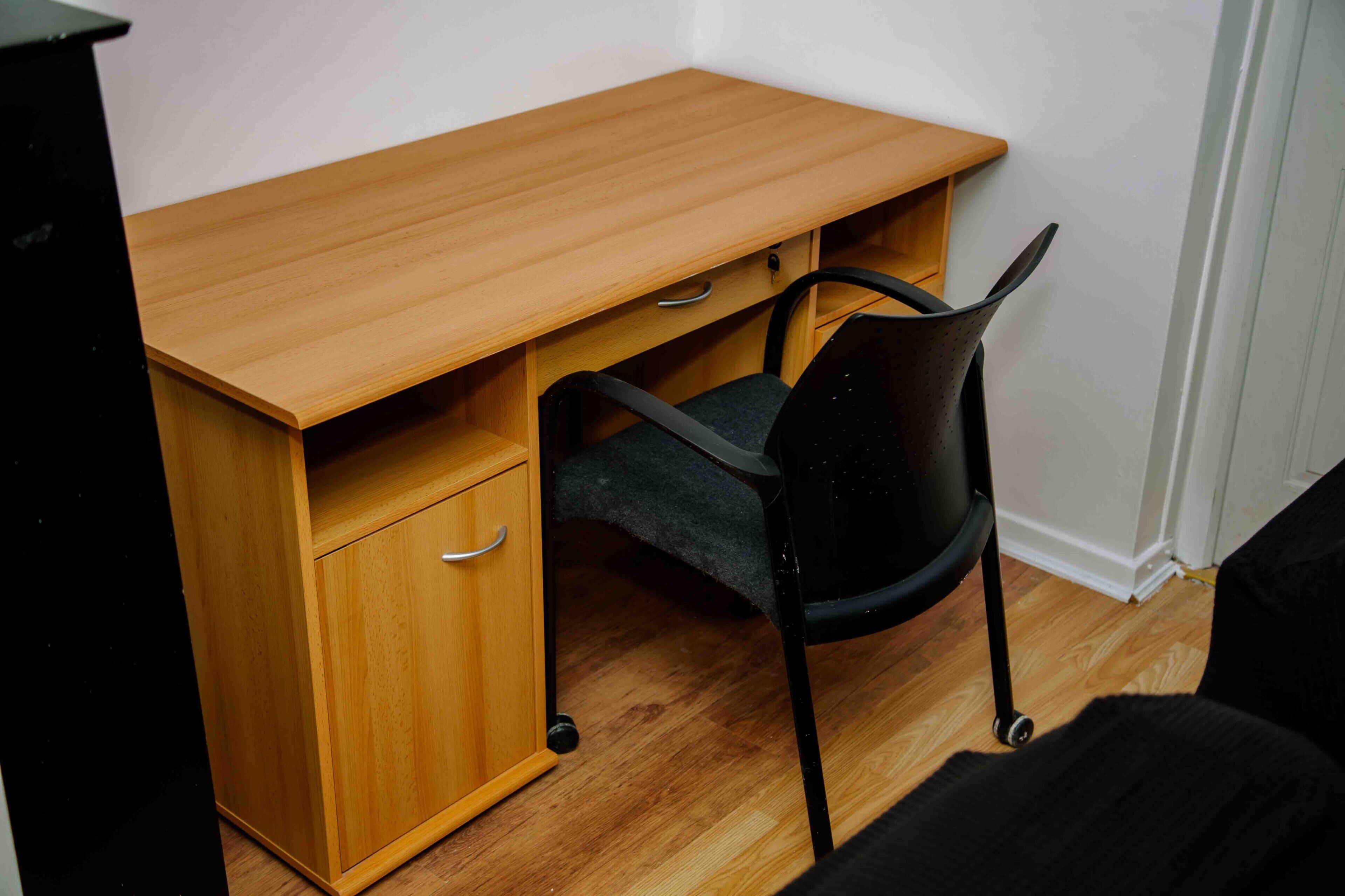 A wooden desk with a chair, a drawer, and a small shelf.