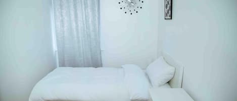 A bedroom with a bed, a bedside table, a wall clock, and a curtain.