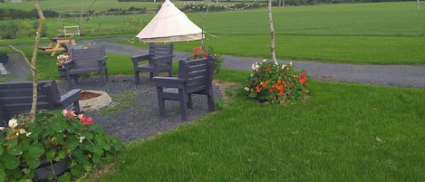 An outdoor seating area with a table and chairs, a small garden with flowers, and a view of a green field.