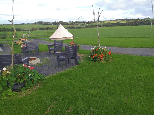Un espace extérieur aménagé avec une table et des chaises, un petit jardin fleuri et une vue sur un champ verdoyant.