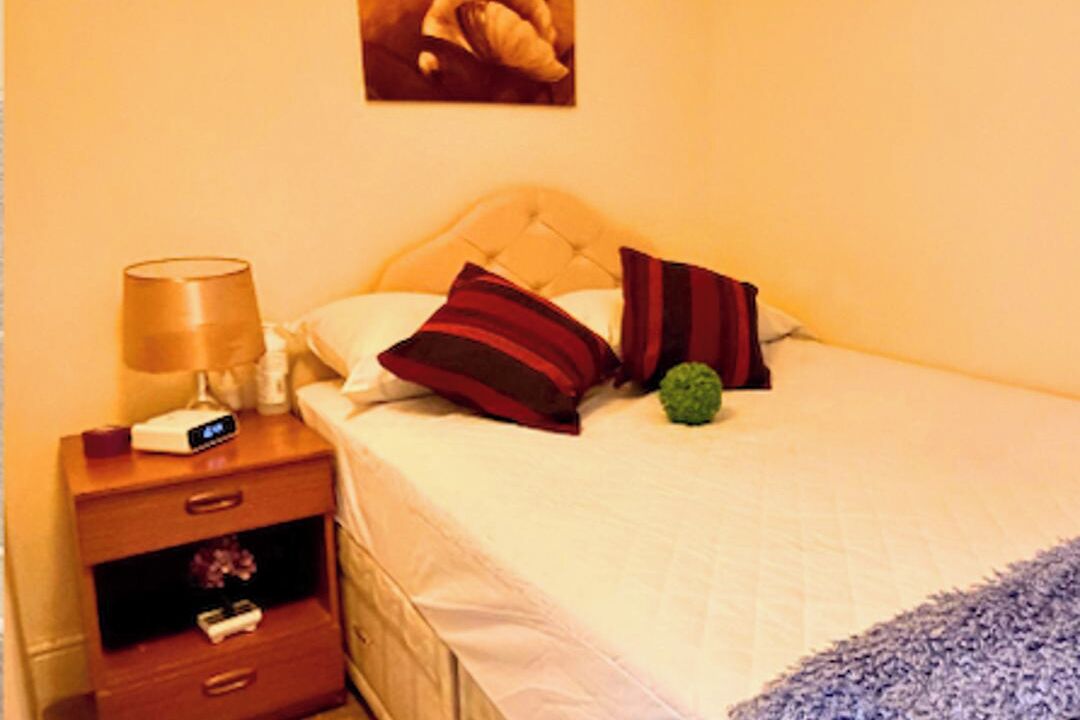 A hotel room with a bed, a nightstand with a lamp, a clock, and a small decorative item.