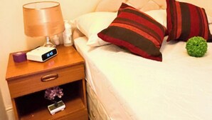 A neatly made bed with pillows and a bedside table with a lamp and a digital clock. - Apartment Sleeps 6 with in Kilburn Lane (London)
