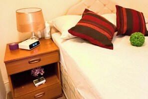 A neatly made bed with pillows and a bedside table with a lamp and a digital clock. - Apartment Sleeps 6 with in Kilburn Lane (London)