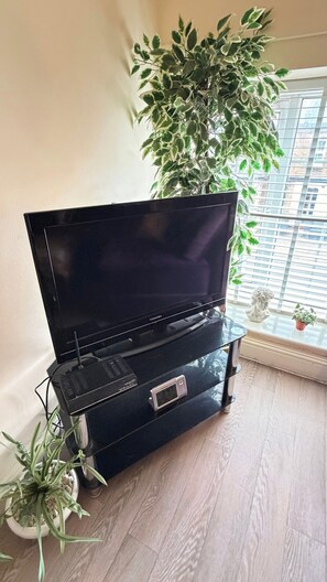 A black entertainment unit with a flat-screen TV, a clock, and a small speaker. - Apartment Sleeps 6 with in Kilburn Lane (London)