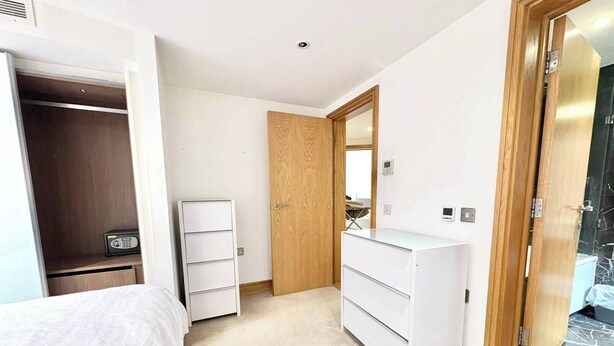 Ein Schlafzimmer mit Bett, Kleiderschrank, Kommode und einer Tür zu einem anderen Raum.
