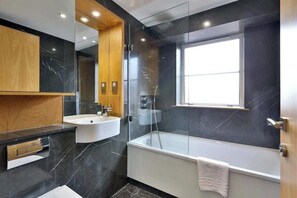 Ein modernes Badezimmer mit Badewanne, Waschbecken, Spiegel und Fenster.