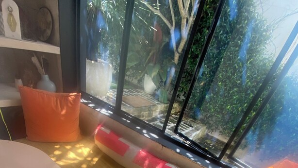 A room with a round table, a vase with flowers, and a window with a view of greenery. - Bronte garden apartment (Waverley)