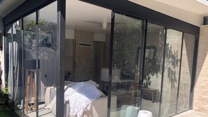A modern bedroom with a glass wall, a bed, a bedside table, and a lamp. - Bronte garden apartment (Waverley)