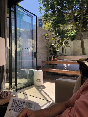A room with a glass door leading outside, a wooden bench, a potted plant, and a white barrel. - Bronte garden apartment (Waverley)