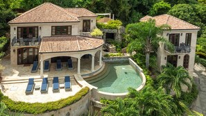 A large house with a swimming pool, a covered patio, and multiple lounge chairs. - VILLA AMOROSA: Upper Peter Bay Luxury Getaway w/ Ocean Views, Private Pool (St John)