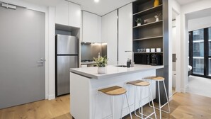 Uma cozinha moderna com uma ilha central, banquetas, forno embutido e máquina de café.