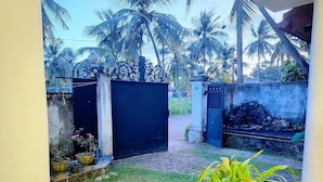 A gated entrance with a paved path leading to a small pond with water lilies, surrounded by potted plants and palm trees. - Serenity Nest Holiday Home, Bollatha Ja Ela, Sri Lanka (Bollate)