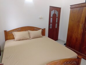Una cama individual con cabecera de madera y dos almohadas, un armario de madera y una puerta con diseño decorativo.