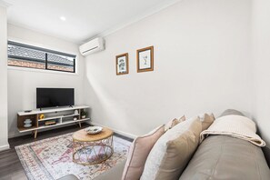 A modern living room with a flat-screen TV, a sofa, a round coffee table, and a patterned rug.