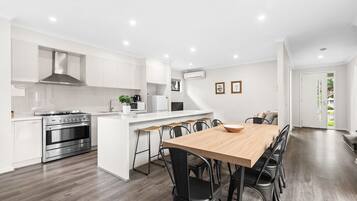 A modern kitchen with white cabinetry, a stainless steel oven, and a wooden dining table with black chairs.