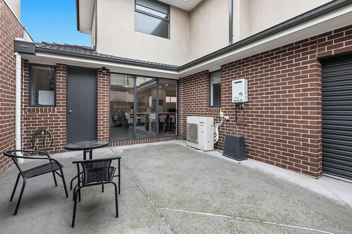 A courtyard with a brick wall, a glass door entrance, a table with chairs, and an air conditioning unit.