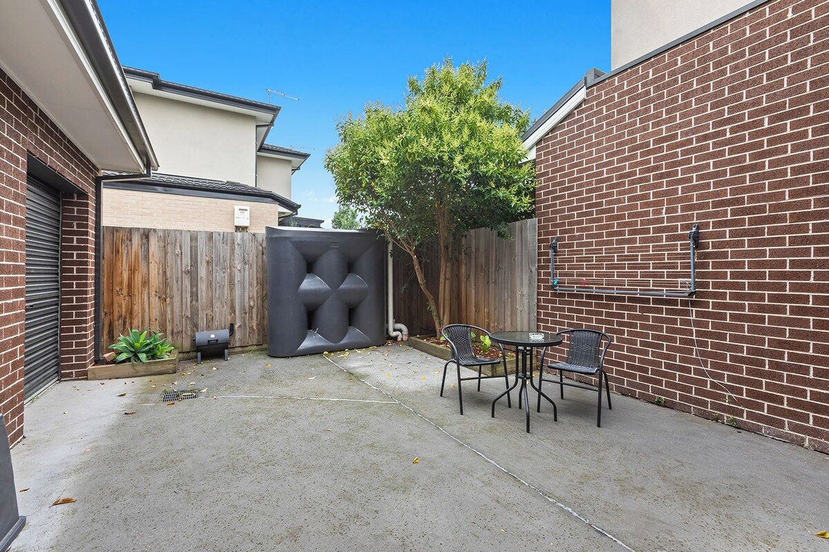 A backyard with a brick wall, a wooden fence, a tree, and outdoor furniture.